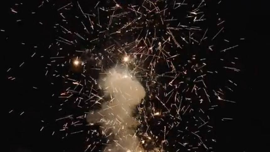 Bright fireworks explode against the dark night sky sending golden sparks and smoke into the air