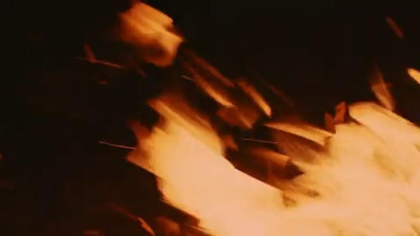 Intense orange flames spread against a dark background with sparks flying in the air