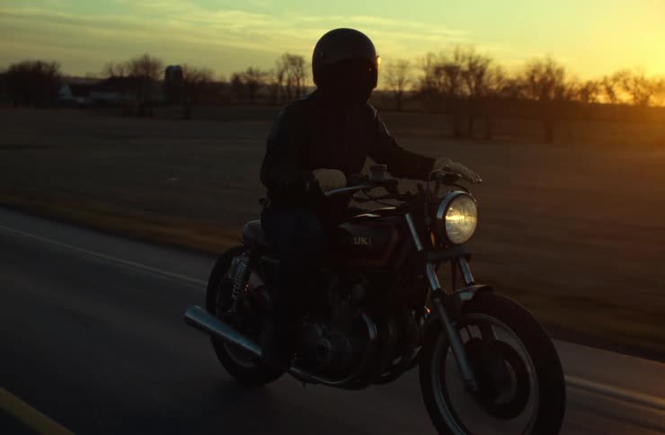 An adult is riding a motorcycle on a rural highway at sunset