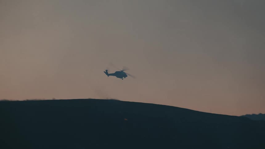 Helicopter descends through a smoky sky over silhouetted hills