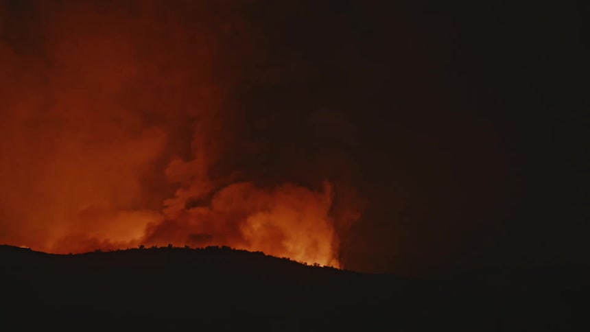 A large fire on a hill one night causing lots of orange smoke to rise into the sky