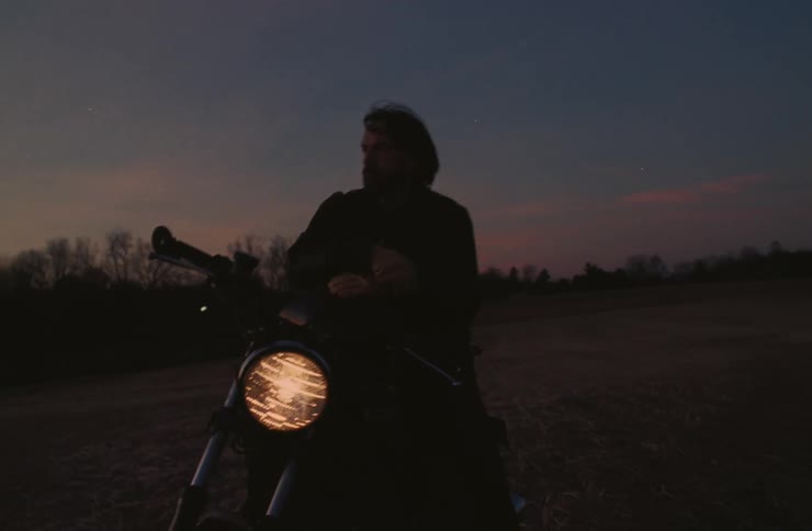 A man gazing in the distance while on a motorcycle on a fall evening