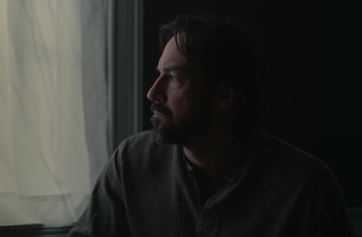 A man in a dark room looks out the window