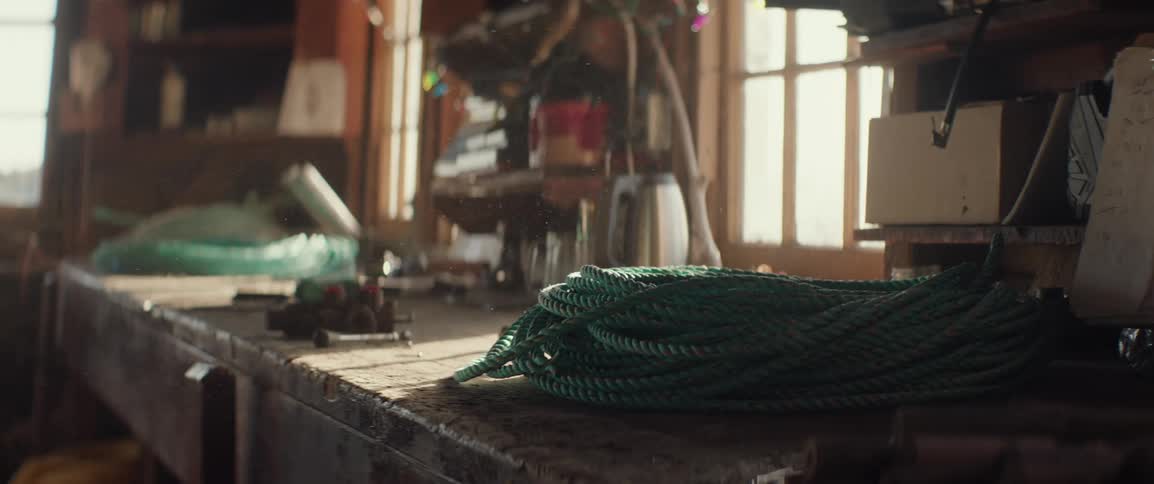 Dust particles glean in the light as a coil of green rope rests on a worn workbench with various tools in a sunlit woodshop