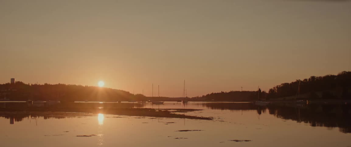 Landscape of a harbor with hills and the sun rising on the horizon