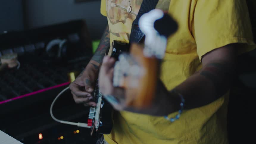 A person in a yellow shirt playing a guitar using his fingers and the person has several tattoos on his arm