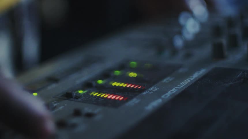 A closeup of an audio mixing console with illuminated led level meters displaying various levels of audio signals