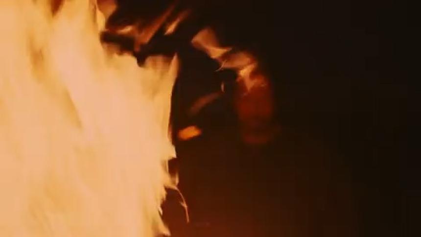 A man stands in the dark watching the flame