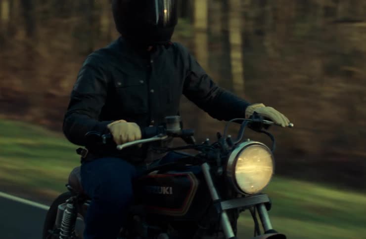 An adult is riding a motorcycle on a rural highway on a sunny winter day