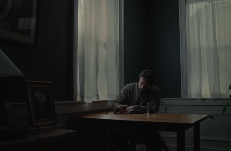 Thoughtful man sitting at the table opening a notebook and starting to write
