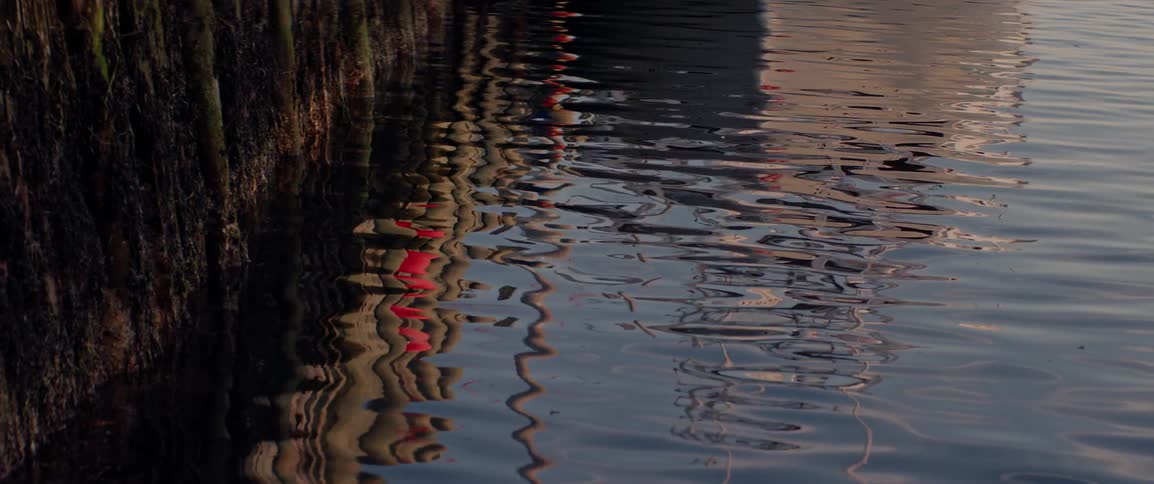 Gentle ripples reflect the image of a docked boat along a quiet waterfront