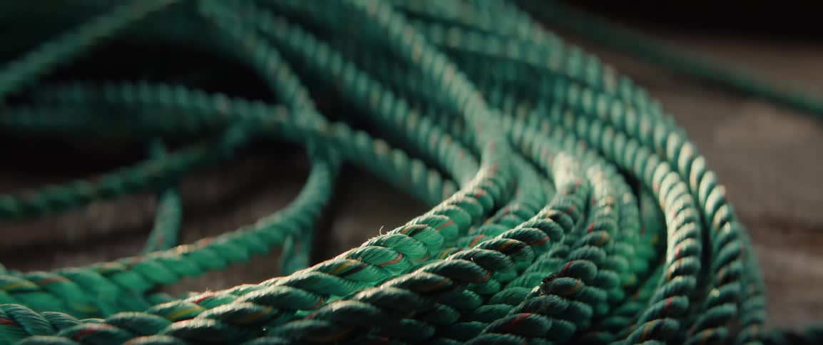 Thick green ropes are coiled and intertwined on a wooden surface