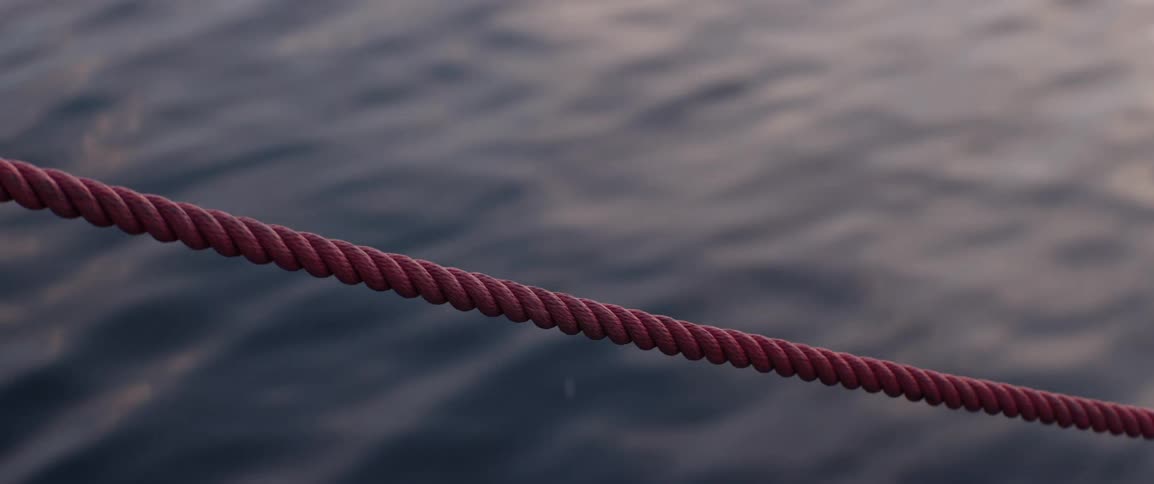 A taut rope sways gently in the wind framed against rippling water reflecting the warm hues of sunset