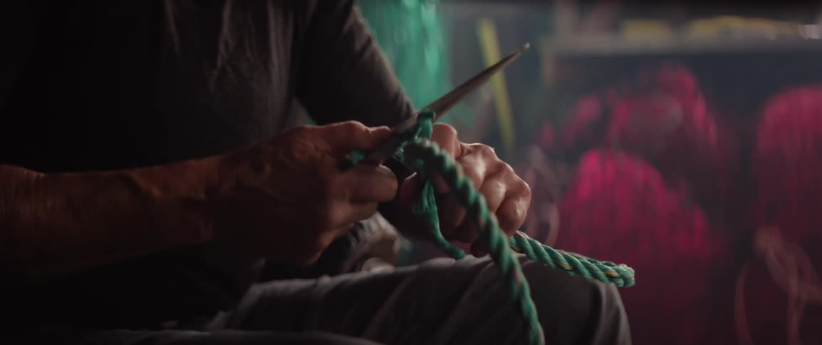 Person cuts a thick green rope with a knife