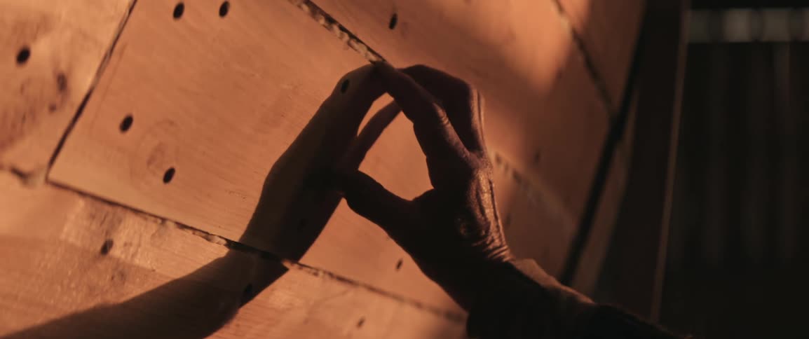 A persons hand passing over the surface of a wooden boat making a shadow