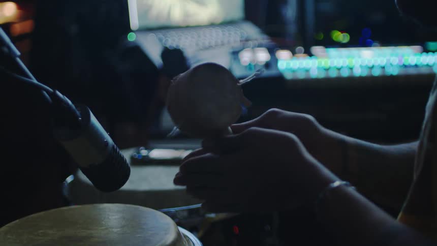 A persons hand holding a small drum next to a microphone