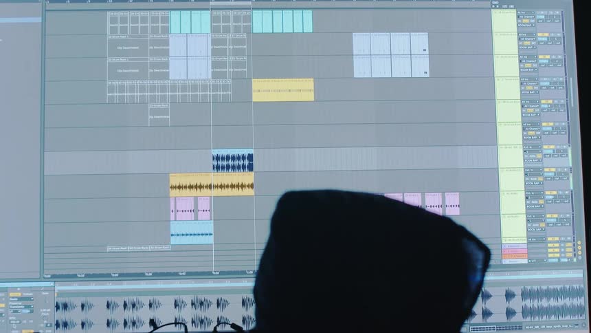 A big screen with music player software and a hooded person in front looking at it