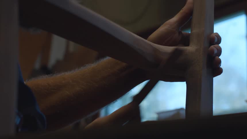 Hand of a carpenter with a sandpaper sanding the corner of a piece of wood