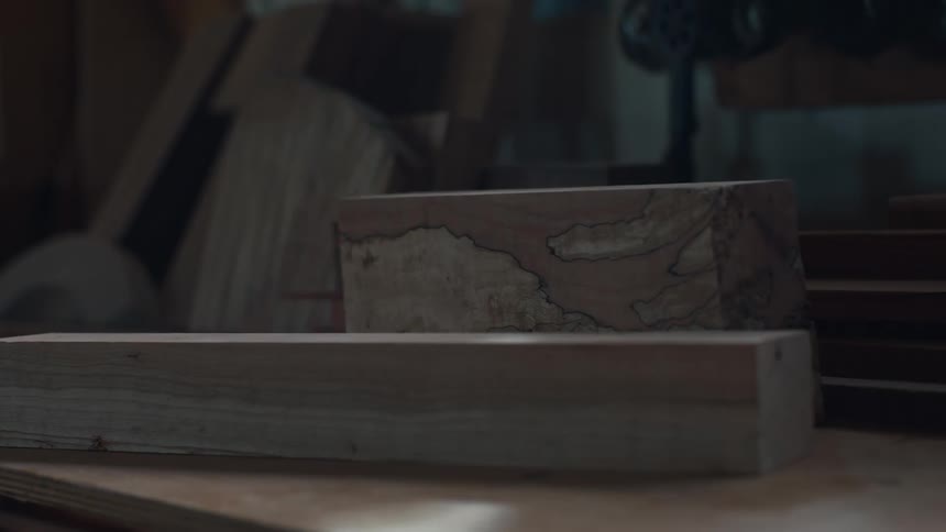 Two rectangular blocks of wood are stacked with the top block featuring a unique swirled pattern in a dimly lit workshop setting