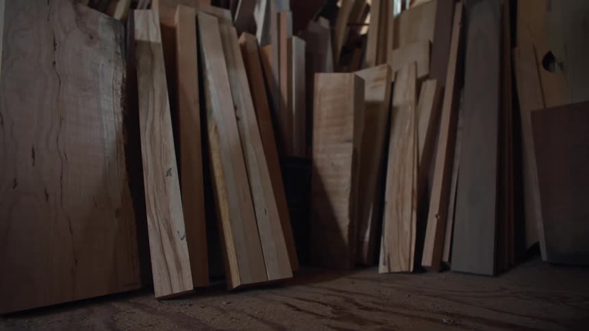 A collection of various wooden planks are stacked vertically in a slightly angled arrangement in the corner of a room