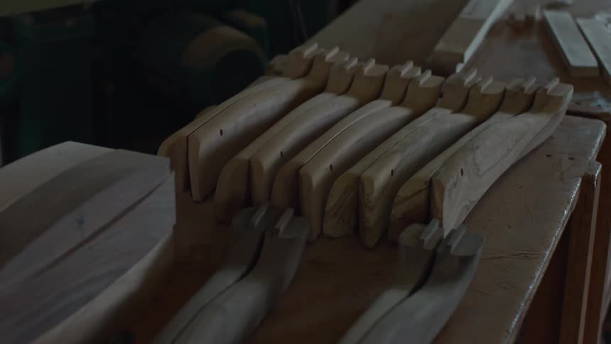 A dimly lit woodworking shop featuring neatly arranged partially carved wooden pieces on a workbench ready for further crafting