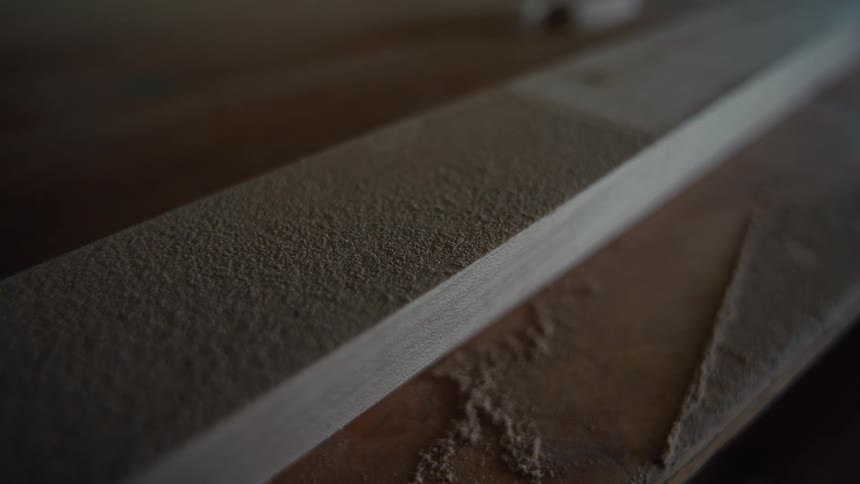 A closeup shot of a wooden plank shows a fine layer of sawdust on its surface