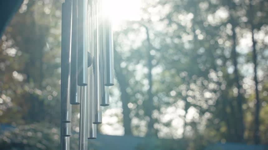 Metal tube wind chime hanging outdoors with trees in the background