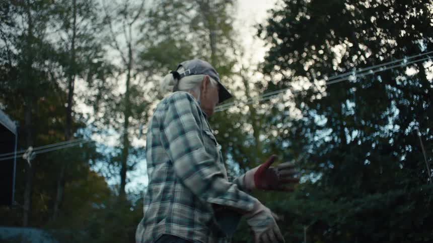 Elderly lady turning over a construction cart and removing dirt from it in her backyard