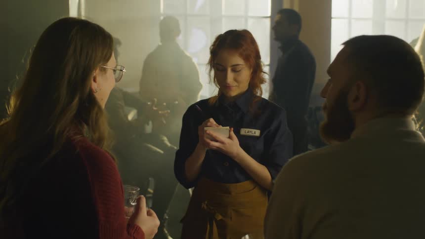 A server takes an order from customers in a dimly lit restaurant