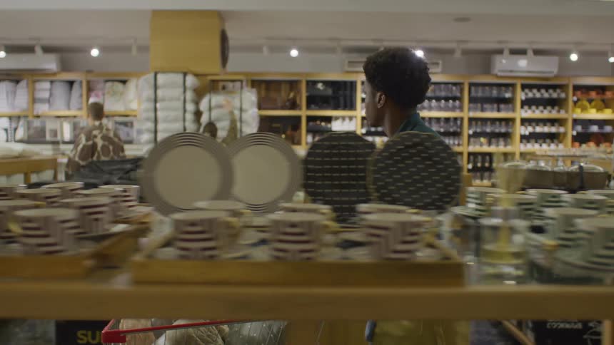 An employee pushes a shopping cart filled with blankets through a wellorganized store selling kitchenware and home goods with shelves stocked with pots pans and dishes