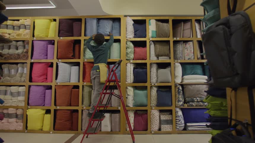 Employee stocking pillow on top shelf in retail store