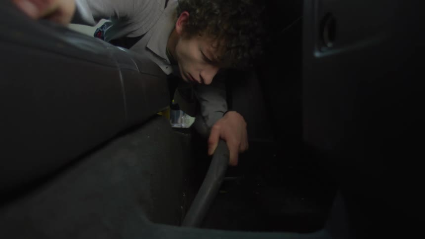 A young man is vacuuming the car floor at night