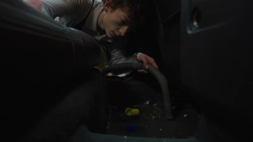 Young man vacuuming dirt from the back of a vehicle