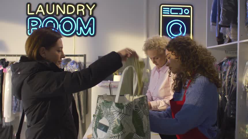 Employees in a laundry room receive clothes and write a receipt for a customer