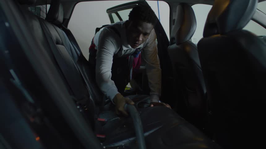 Man in apron vacuuming the back seats of a vehicle
