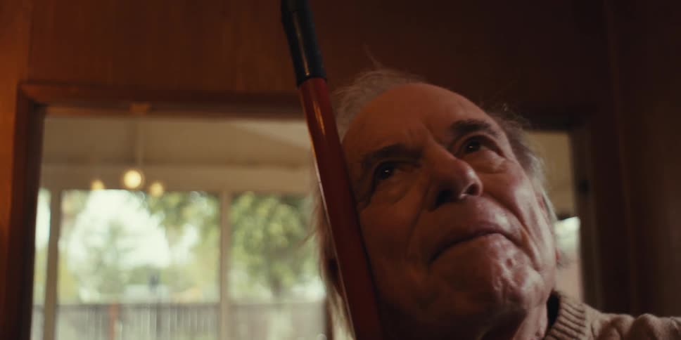 A happy elderly man smiles while dancing alone at home with a cane