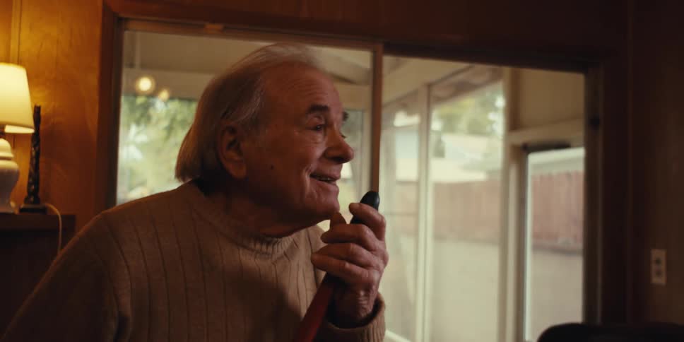 Elderly man dancing and singing in living room while cleaning with a broomstick