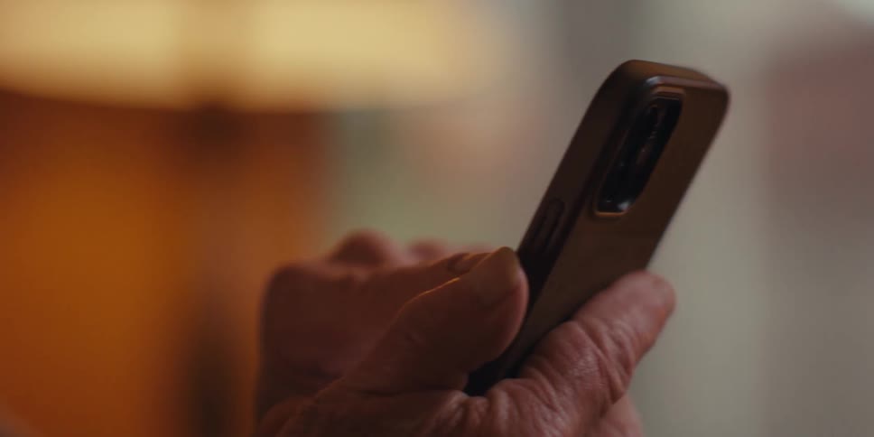 Close up of an elderly man smiling while browsing a phone in a cozy room at home