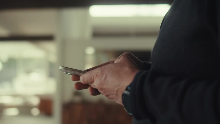 A middle aged man with a dark jacket uses a silver smartphone