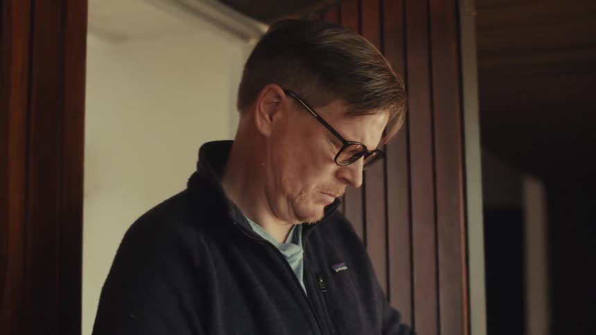 Man walks through a wooden paneled door while looking at the package he is carrying