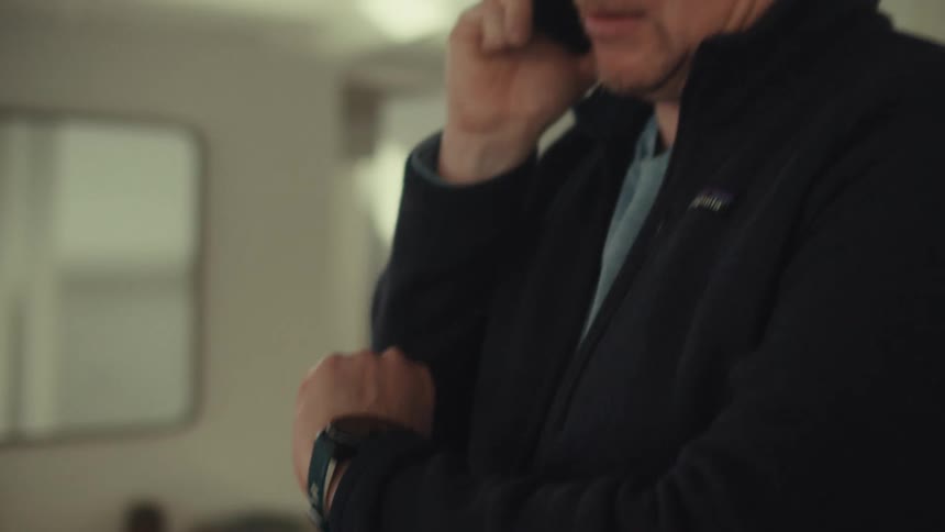 Man talking on a smartphone while standing indoors checks his wristwatch
