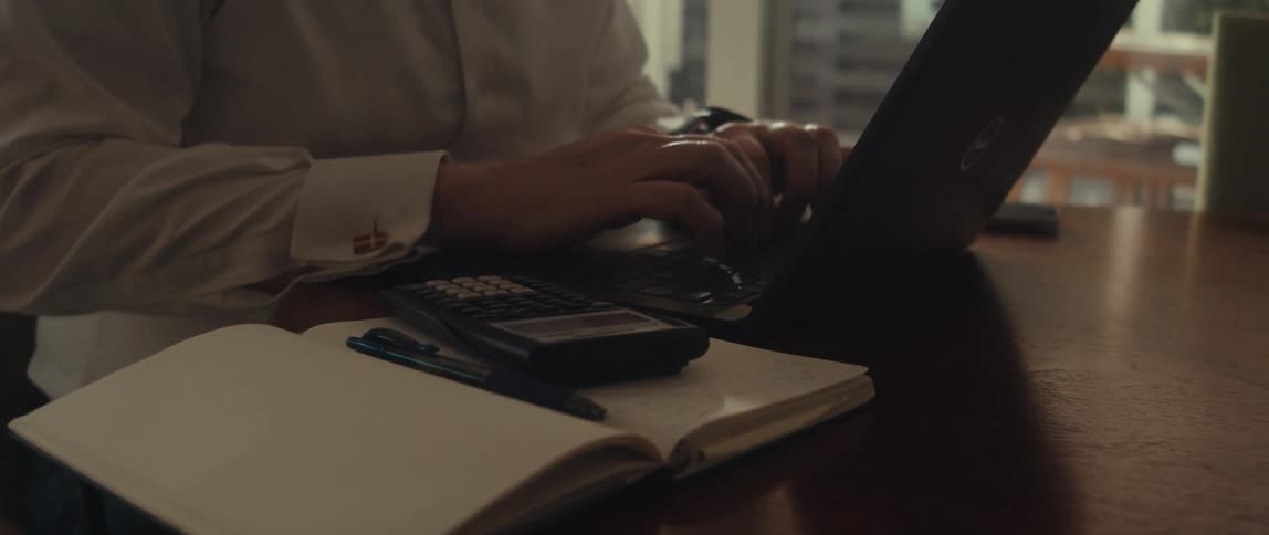 Hands of a man in a white shirt type on a calculator and a laptop