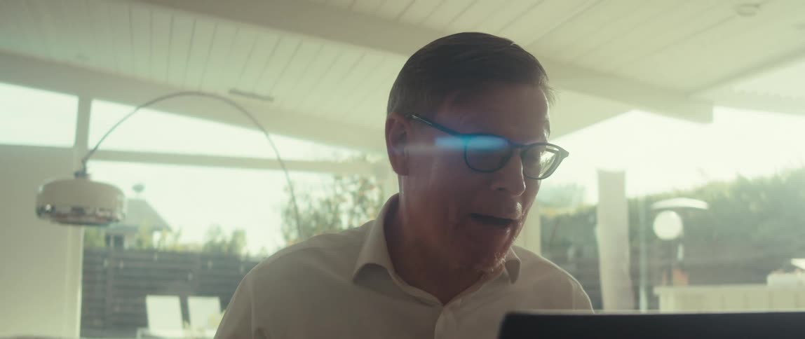Man in glasses and a white shirt smiles slightly as he looks at a laptop screen