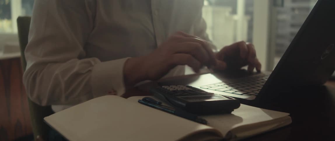 Man in white shirt typing on a calculator and laptop