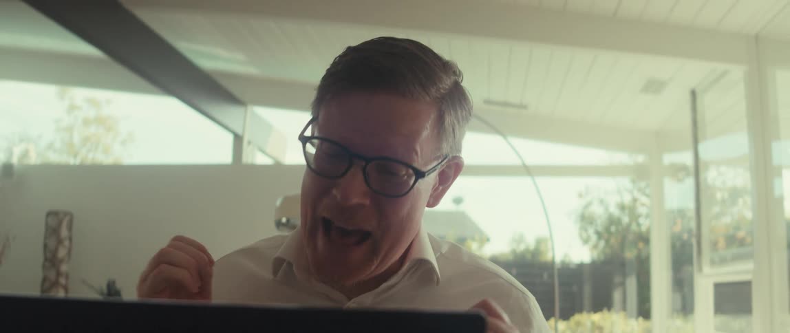 Man with glasses and a white shirt talks in front of a laptop
