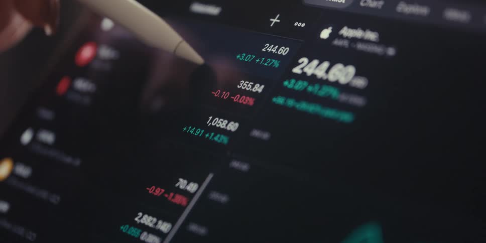 A digital pen pointing to financial data displayed on a screen with stock information for apple and other companies visible suggesting market analysis or trading