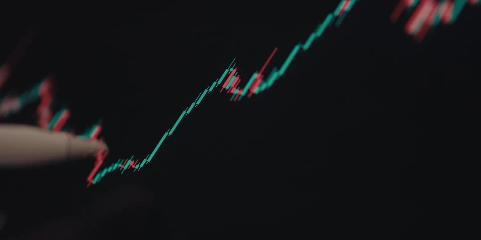 A stylus pen resting against a computer screen displaying a stock market chart with red and green lines