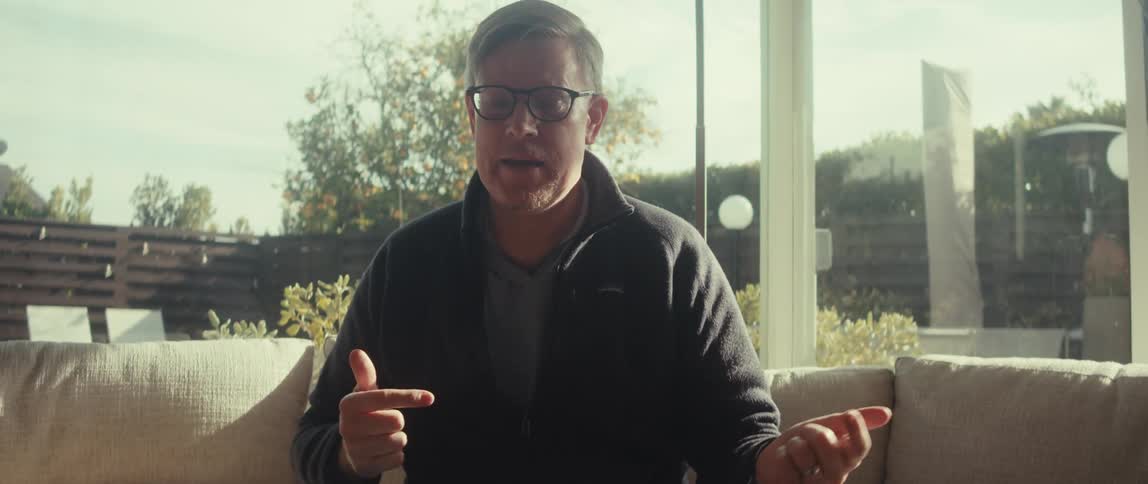 Man wearing glasses gestures while looking at a tablet on the table