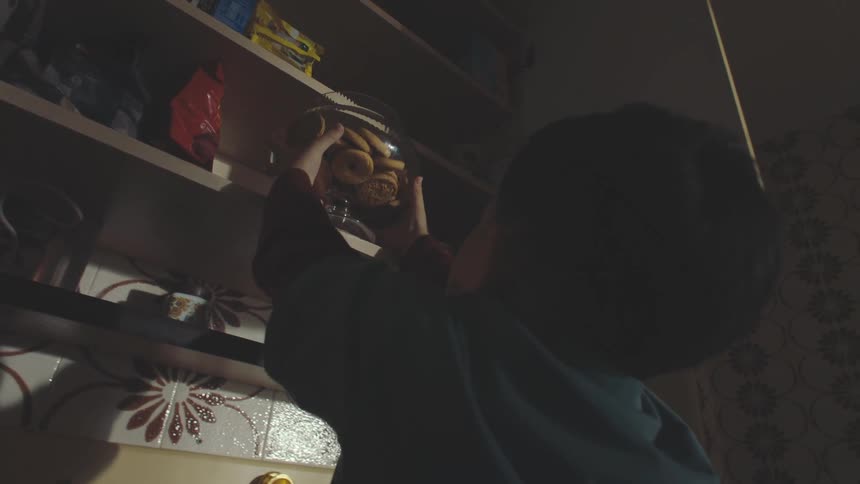 Boy taking a bowl of cookies from a cupboard and handing it to another girl