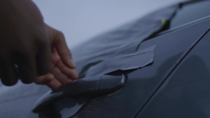 Pair of hands sticking gray tape to a plastic garbage bag covering a car window